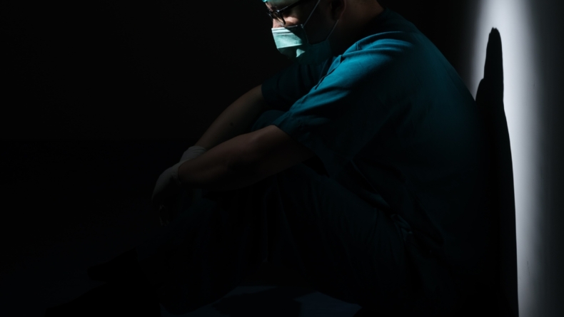 pracownik medyczny siedzący pod ścianą w ciemnym pomieszczeniu